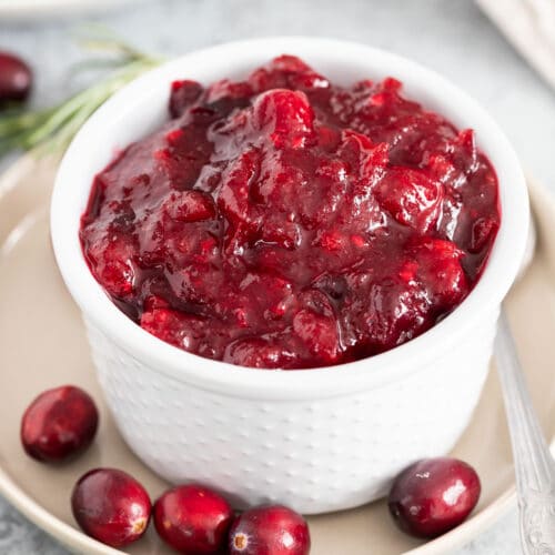 A close up of cranberry sauce in a small bowl garnished with whole cranberries and a spoon next to it.