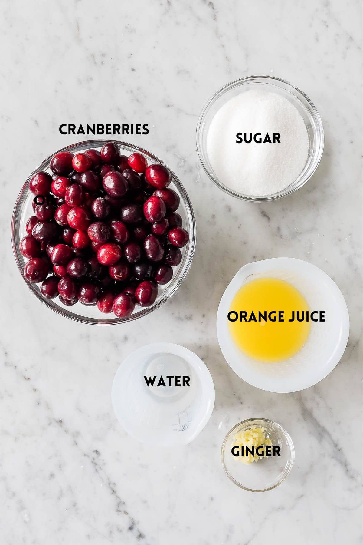 Ingredients needed for cranberry sauce in small bowls on a marble surface.