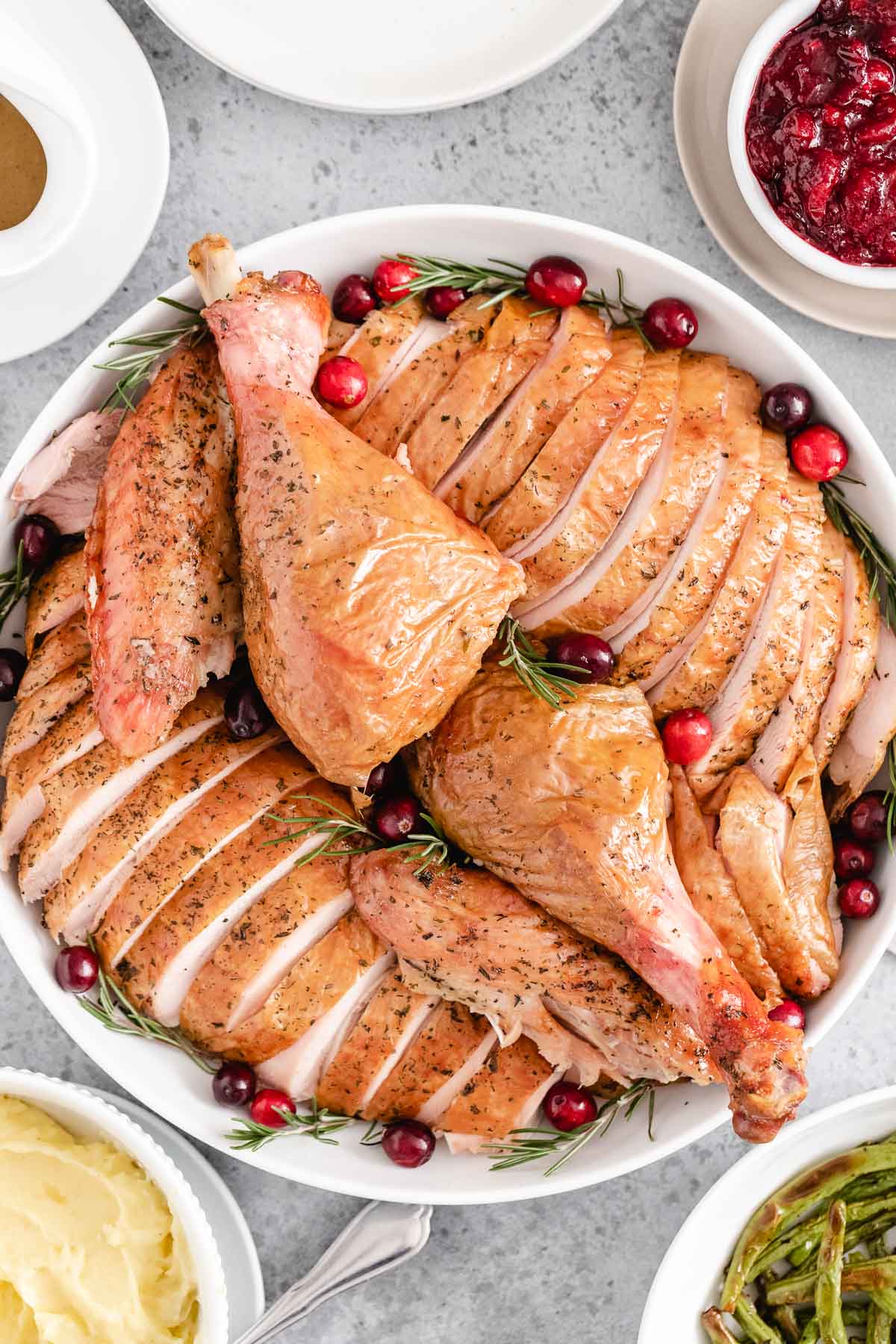 A sliced whole turkey on a white serving platter garnished with cranberries and rosemary.