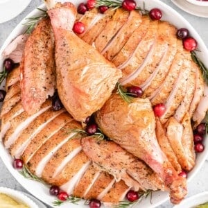A sliced whole turkey on a white serving platter garnished with cranberries and rosemary