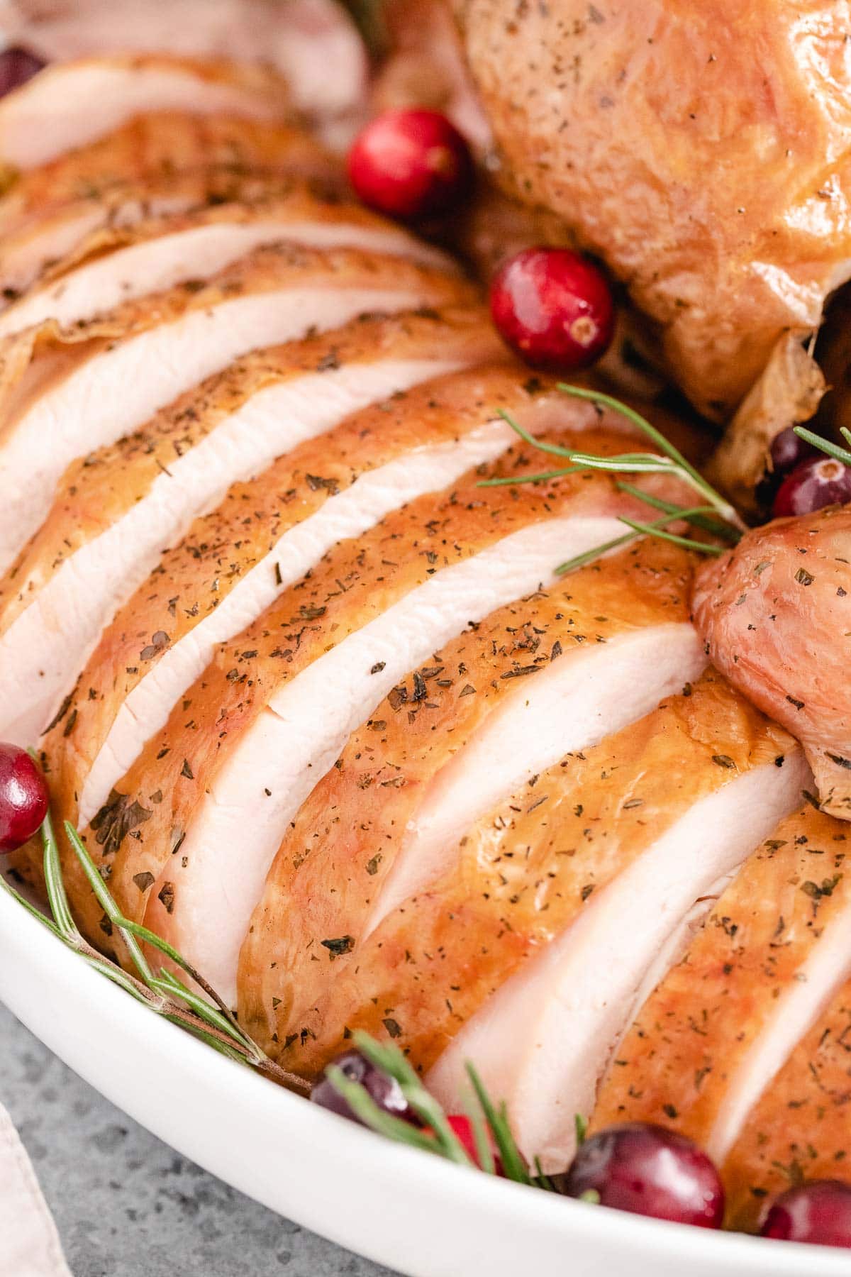 A close up of a sliced turkey breast with the skin on garnished with cranberries and rosemary.