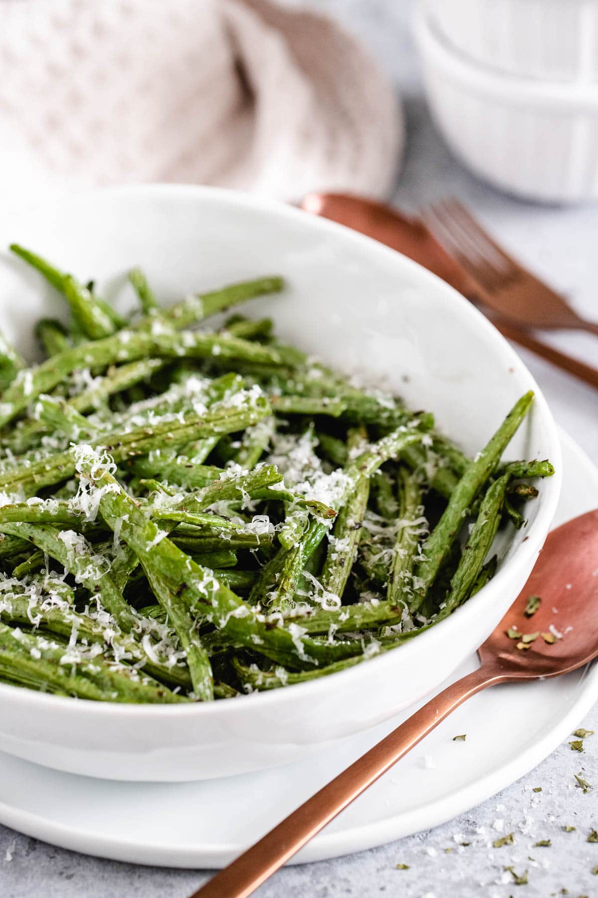 cooked green beans in a white serving dish garnished with grated cheese, next to the bowl is a brown spoon