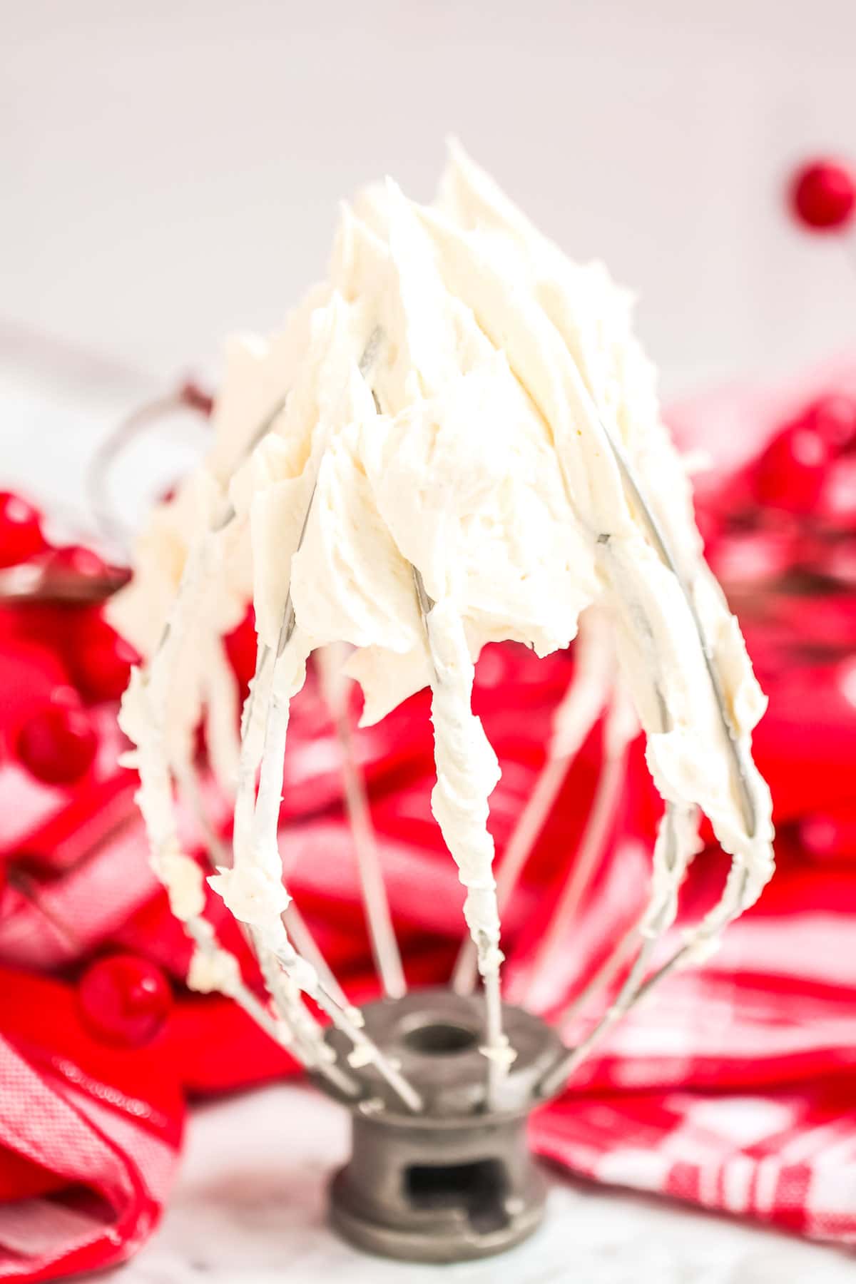a whisk covered with buttercream standing upright in front of a red kitchen towel
