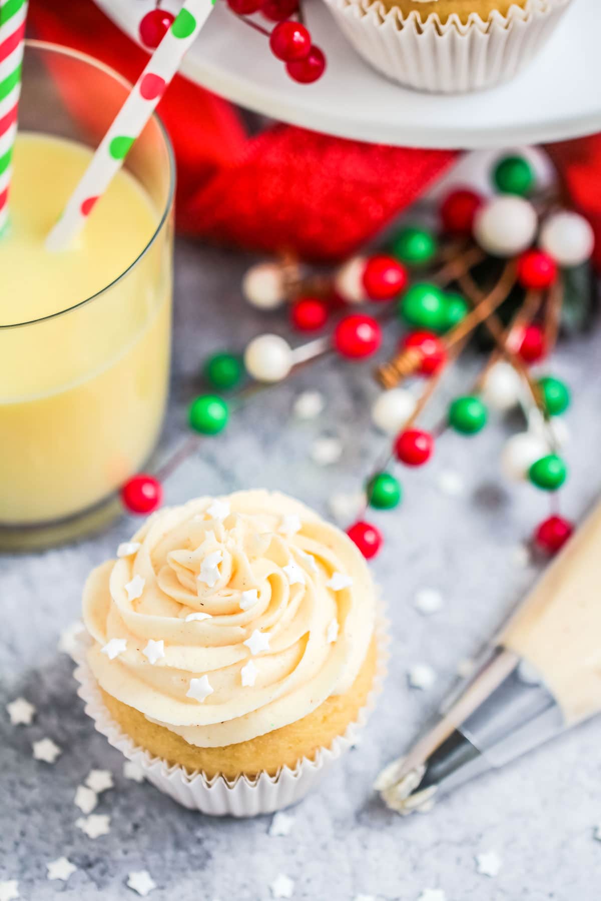 a cupcake next to a glass of eggnog with a straw and a piping bag on a grey surface