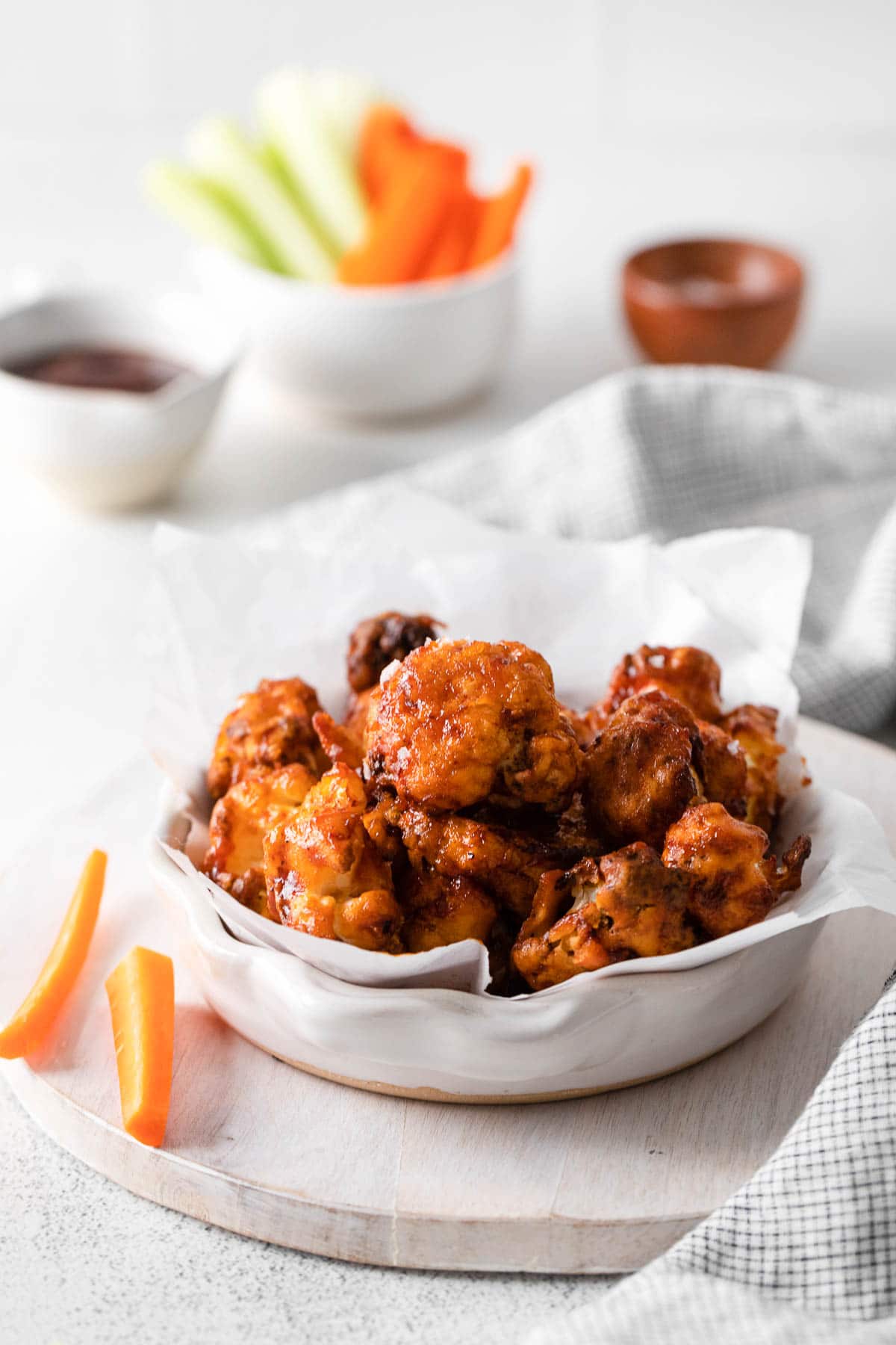 A wooden board with a bowl of cauliflower wings and some carrots