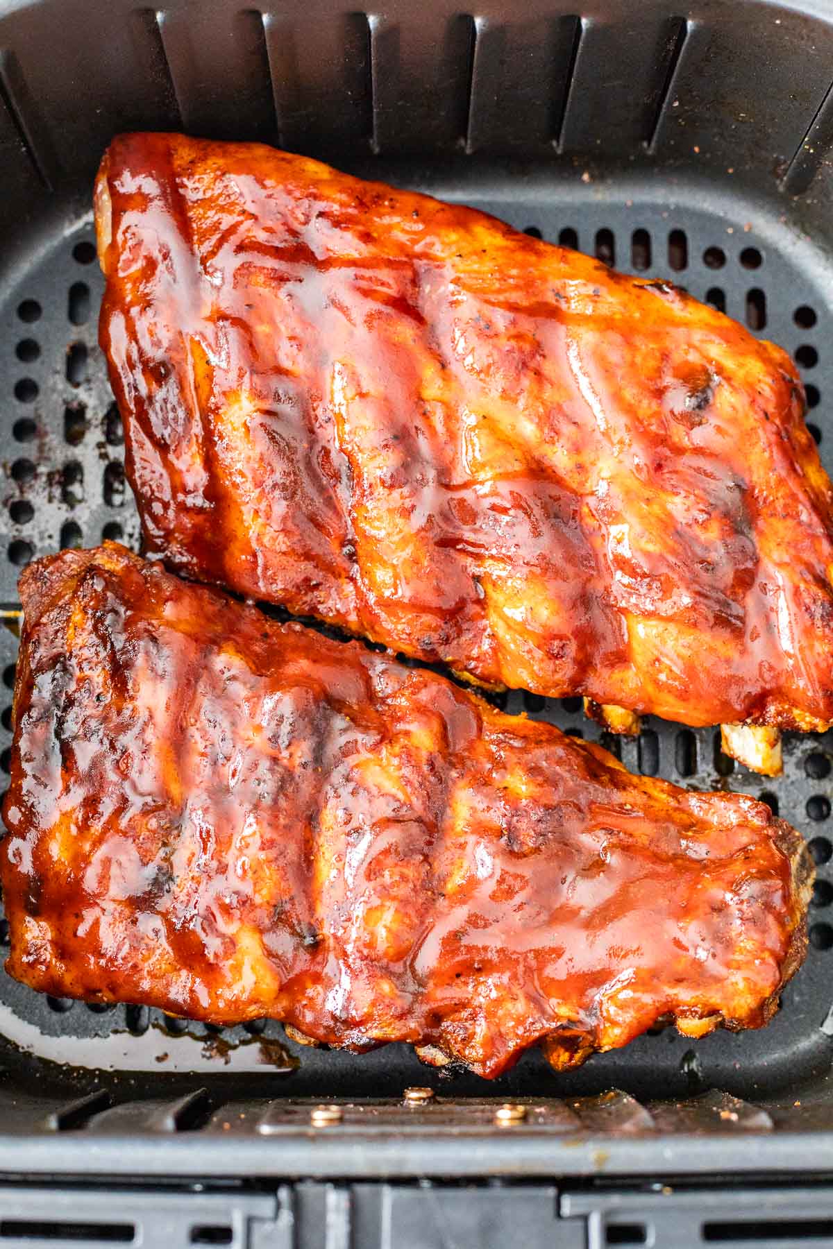 a rack of ribs slathered with BBQ sauce in an air fryer basket