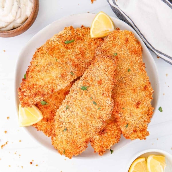 a white plate with air fried breaded fish fillets with lemon wedges, next to a bowl of lemon wedges and a bowl of mayonnaise