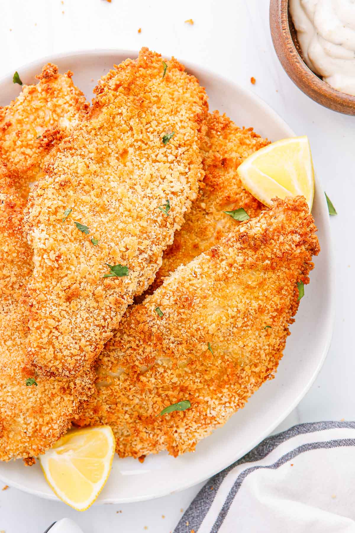 Close-up of a white plate of air fried breaded fish fillets with lemon wedges.
