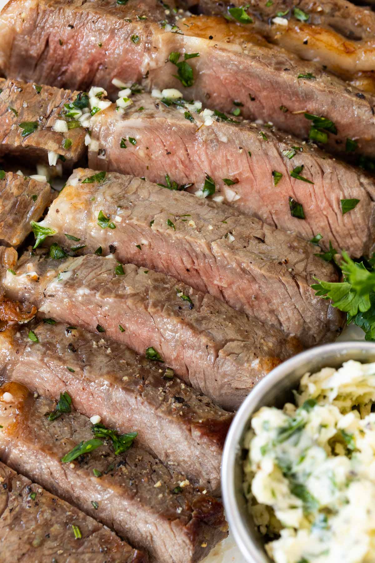 A sliced medium-cooked steak next to a small bowl of garlic butter.