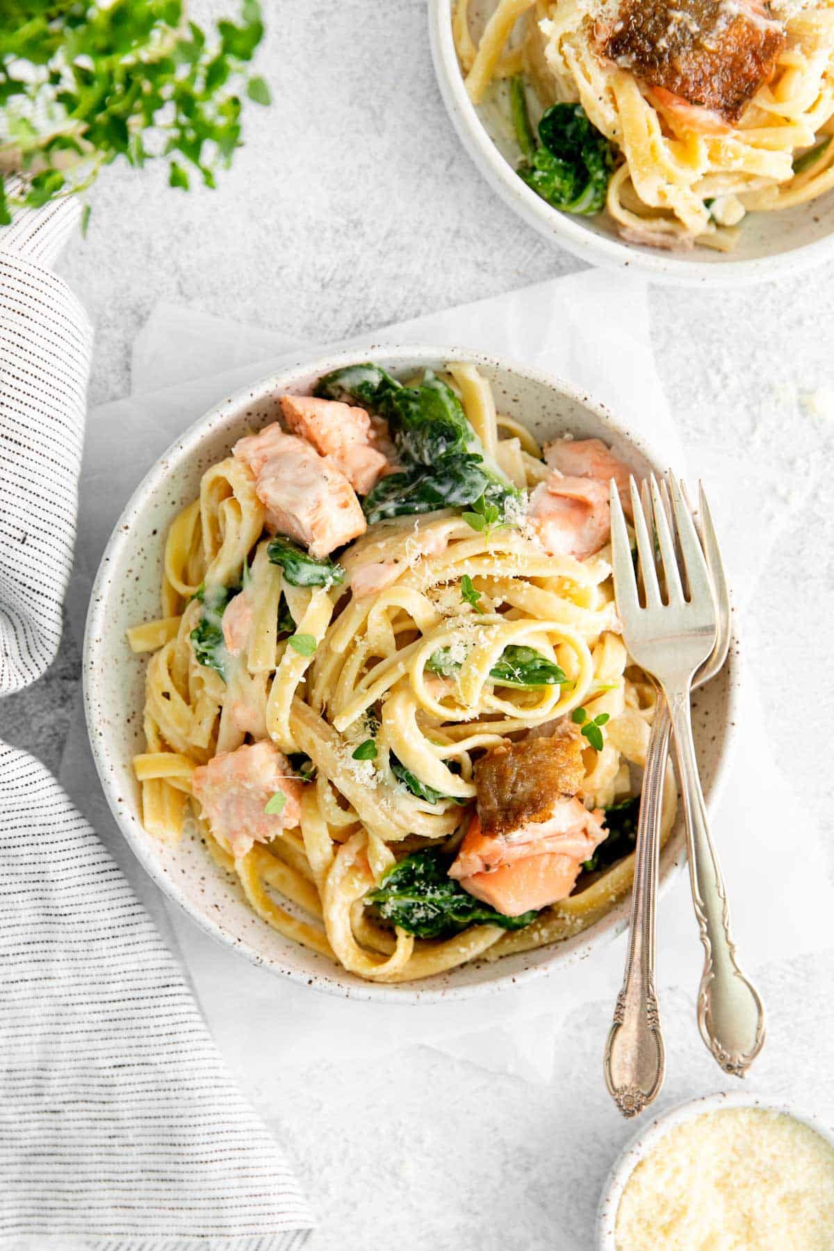 A white bowl filled with salmon pasta with silverware next to it.