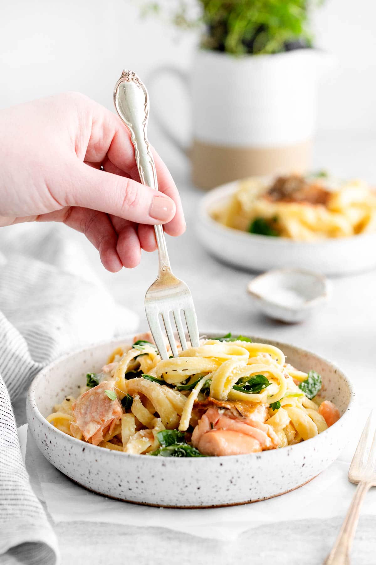 A female hand sticking a fork into a bowl of salmon pasta.