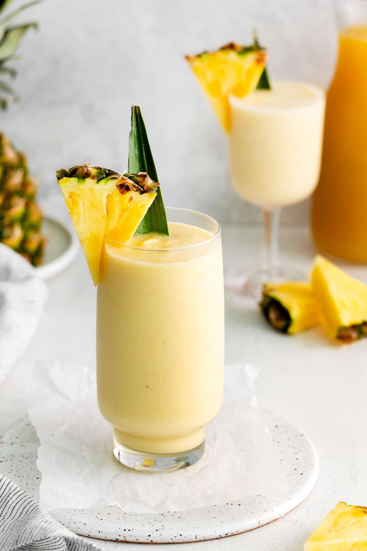 Two glasses filled with a pale yellow drink next to a pineapple.