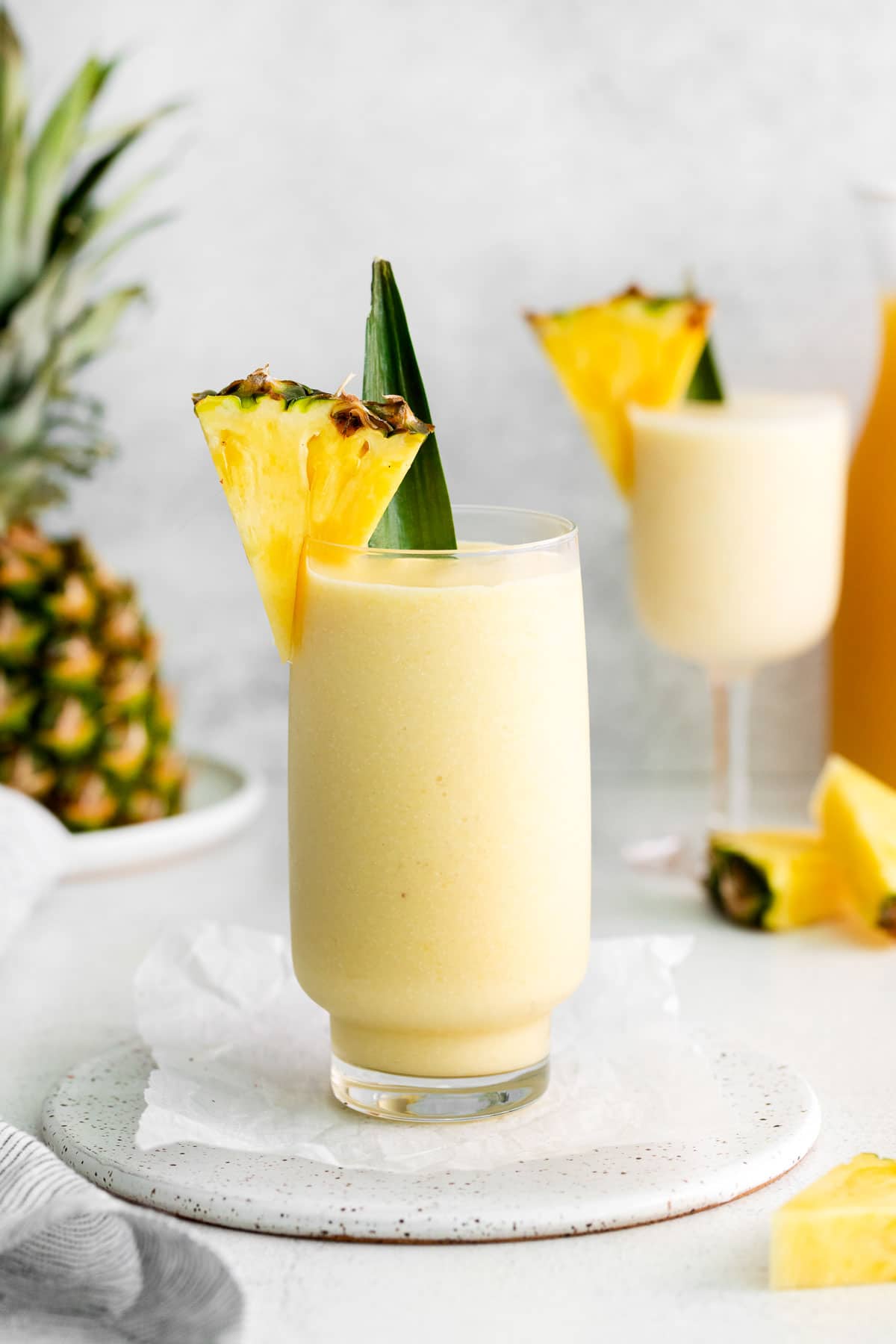 A tall glass filled with virgin pina colada and garnished with a pineapple wedge and leaf.