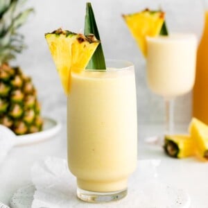 A tall glass filled with virgin pina colada and garnished with a pineapple wedge and leaf.