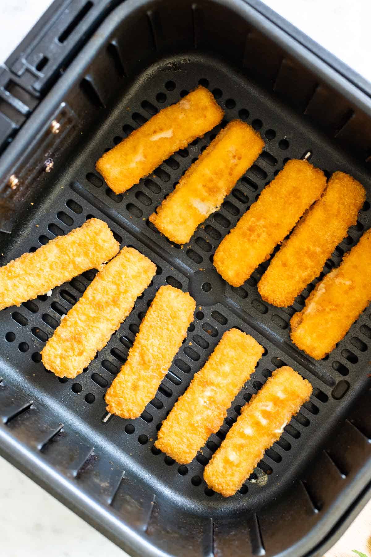 Cooked fish sticks in an air fryer basket.