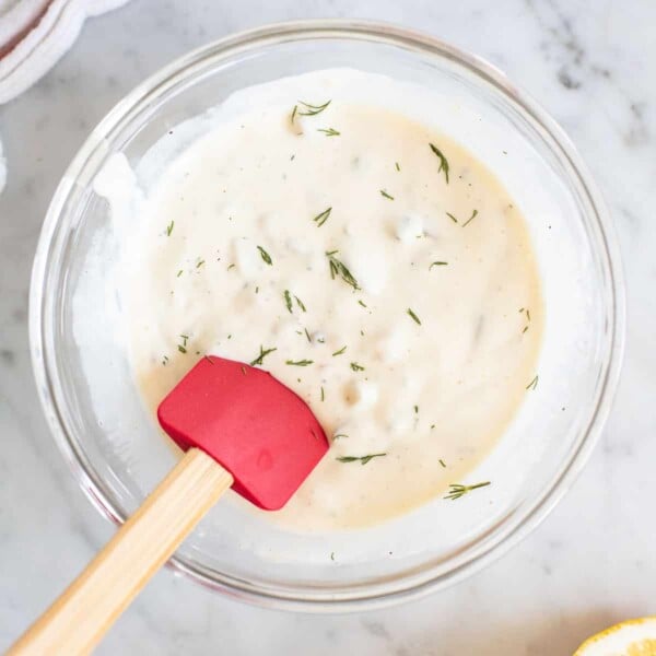 A glass bowl filled with a white sauce and a spatula sticking out.