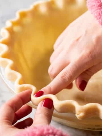 Two hands shaping a fluted pie crust.