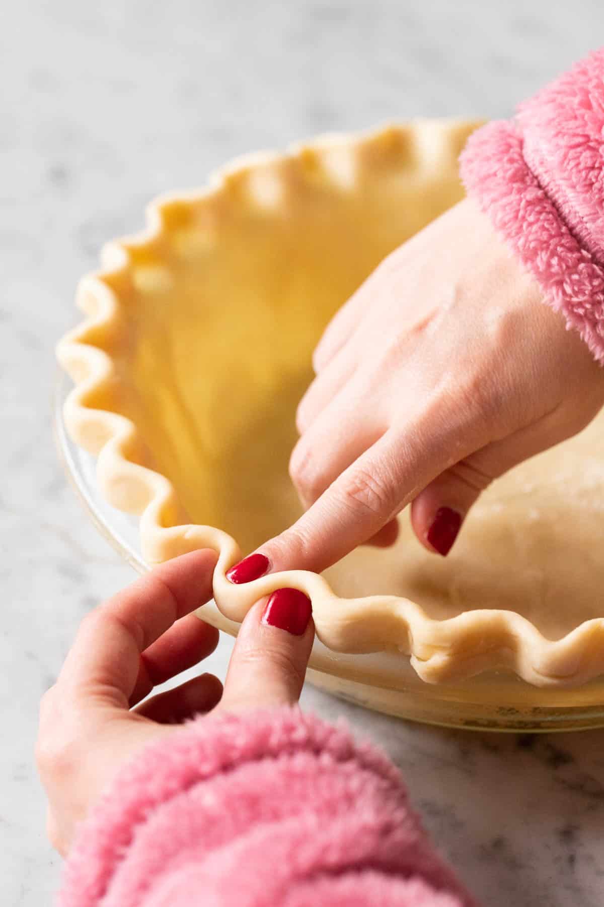 Two hands shaping a fluted pie crust.