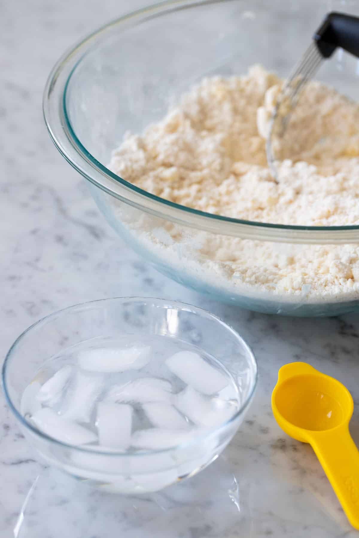A bowl of ice water next to bigger bowl filled with flour and butter.