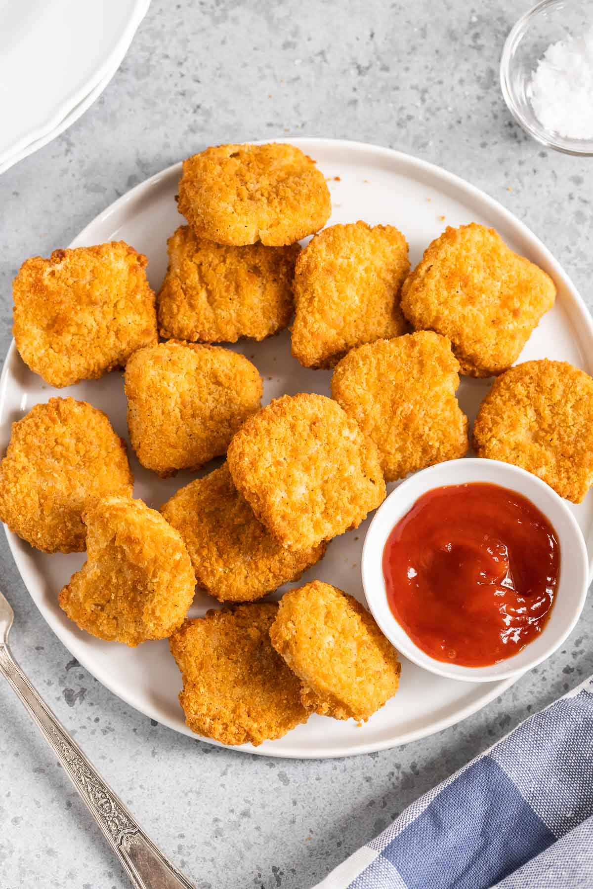 Chicken nuggets on a white plate with a small bowl of ketchup.