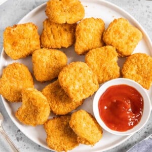 Chicken nuggets on a white plate with a small bowl of ketchup.