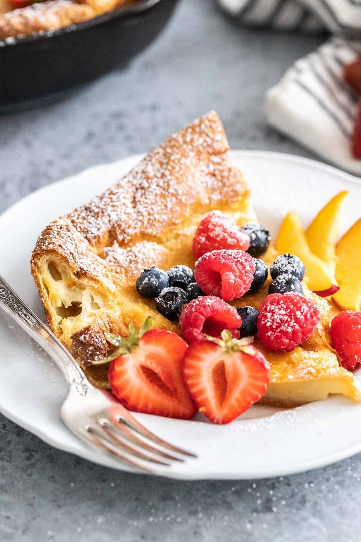 A slice of Dutch Baby pancake on a white plate garnished with berries.