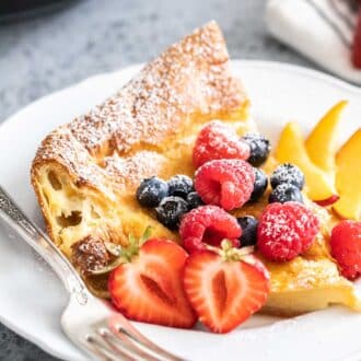 A slice of Dutch Baby pancake on a white plate garnished with berries.