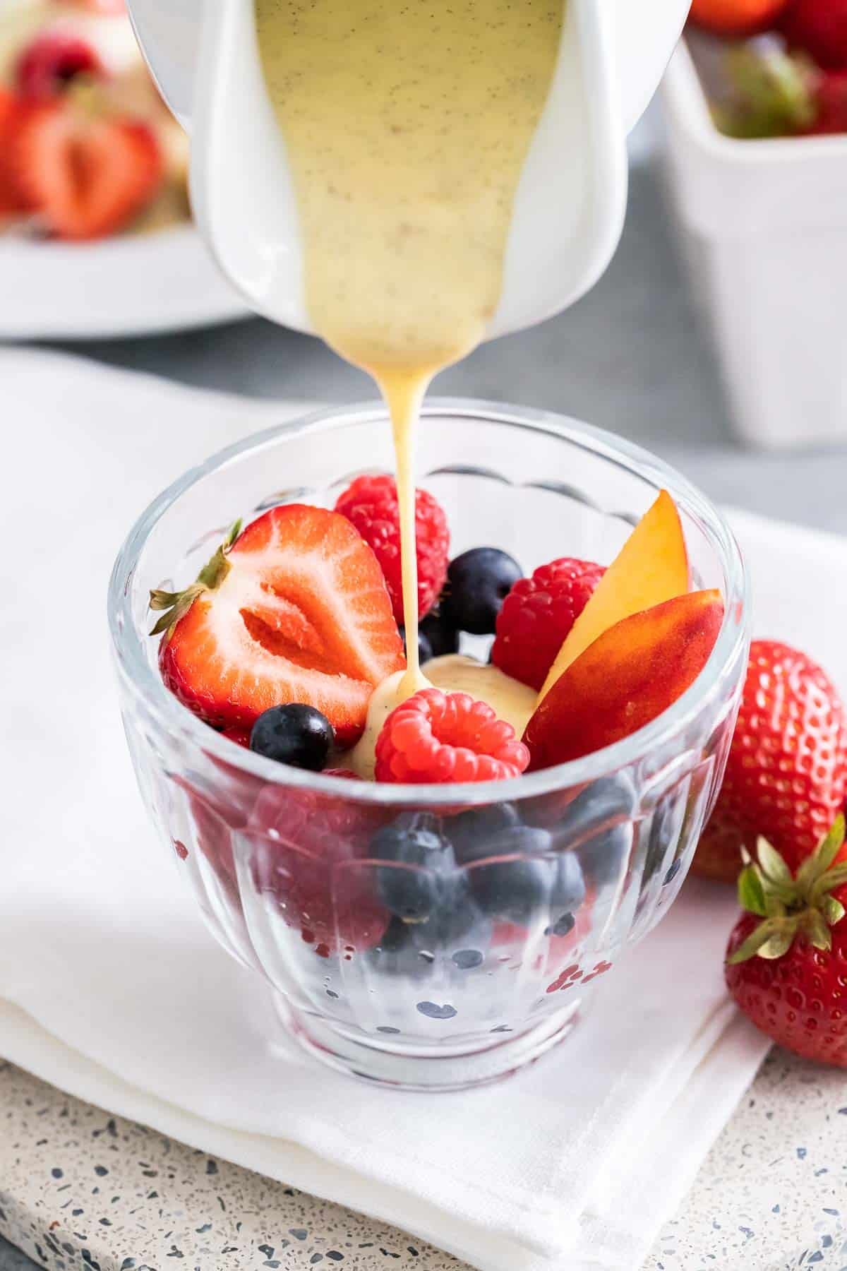 Vanilla sauce being poured over berries in a glass bowl..