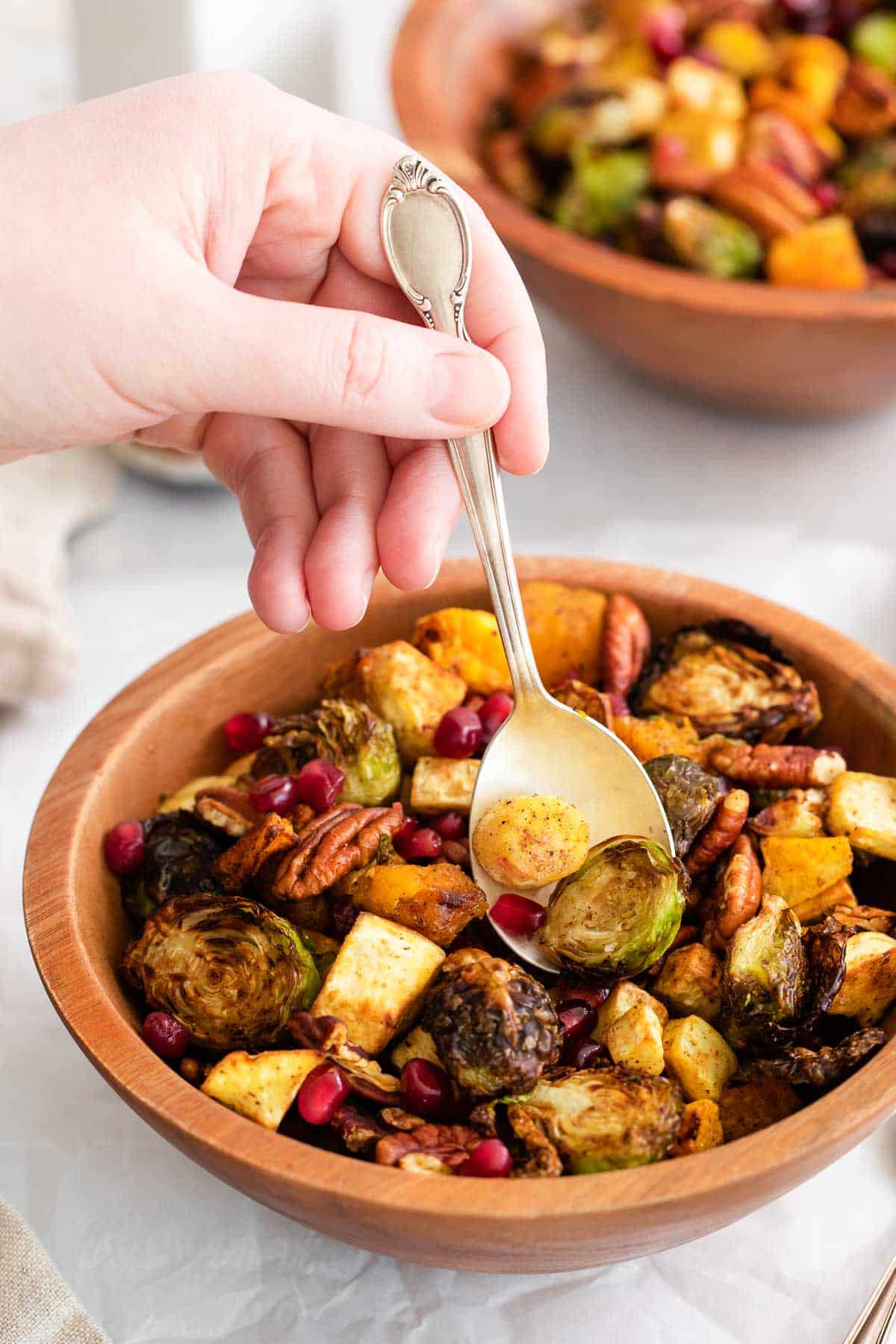 A hand scooping roasted vegetables out of a bowl with a spoon.