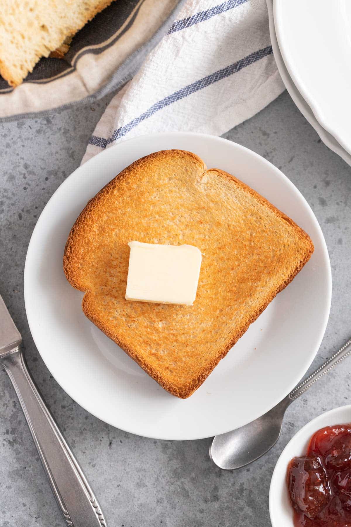 A slice of toast on a plate with a piece of butter on it and a knife next to it.