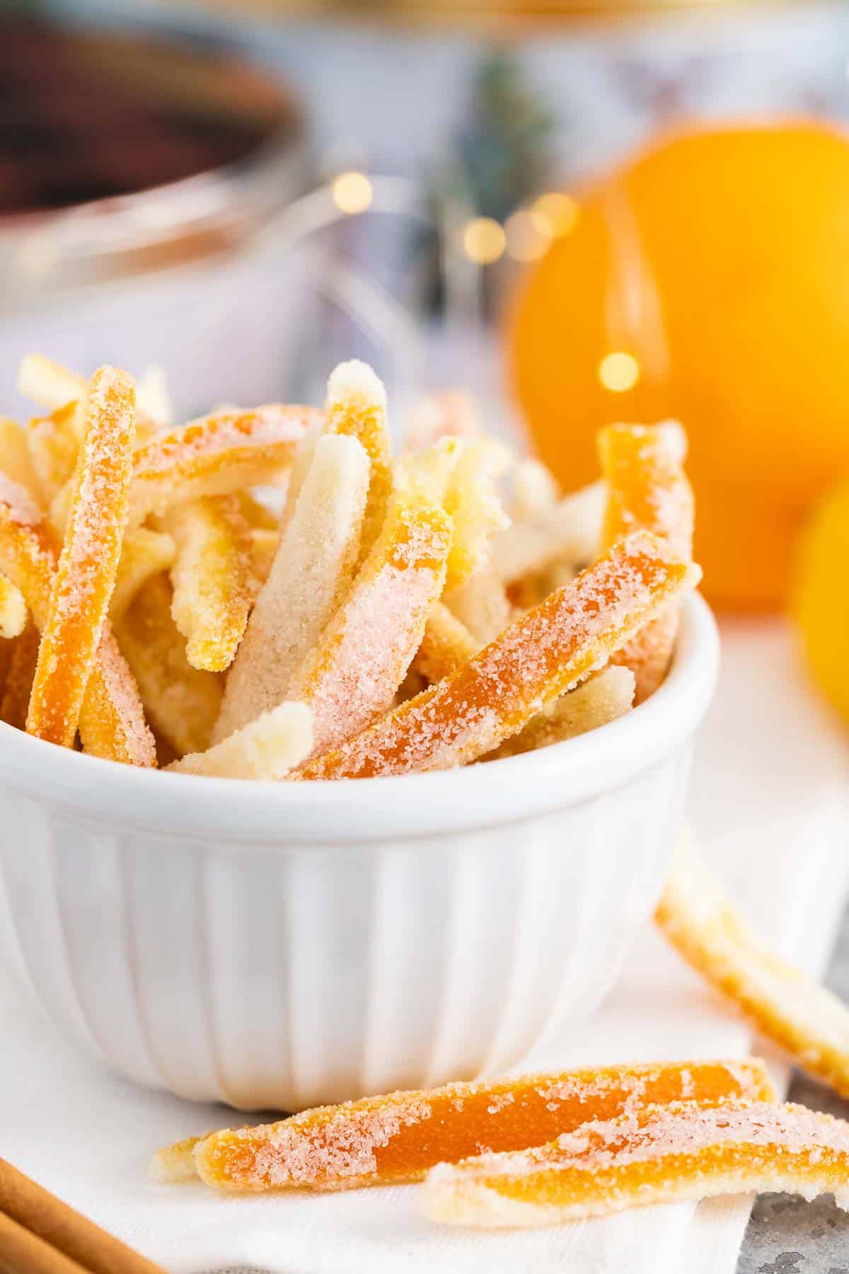 Candied peel in a small white bowl with oranges in the background.
