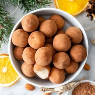 Marzipankartoffeln in a white bowl, next to it are orange slices and almonds.