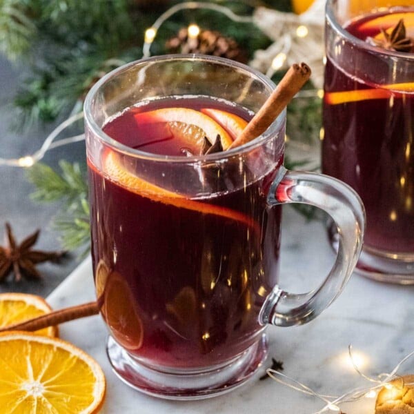 A glass mug filled with Glühwein, garnished with a cinnamon stick and orange slices.