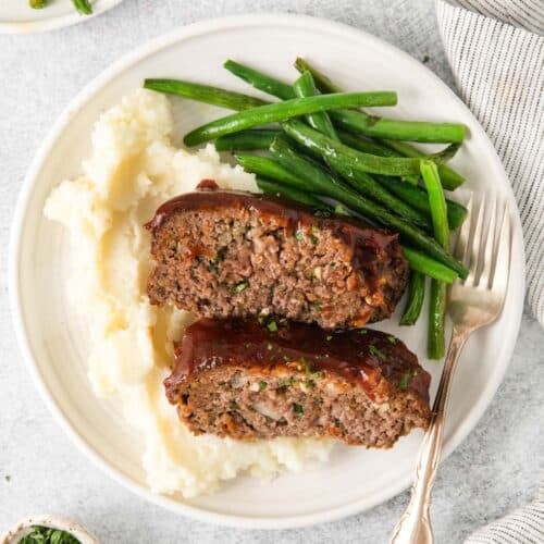 A plate with two slices of meatloaf, mashed potatoes, and green beans.