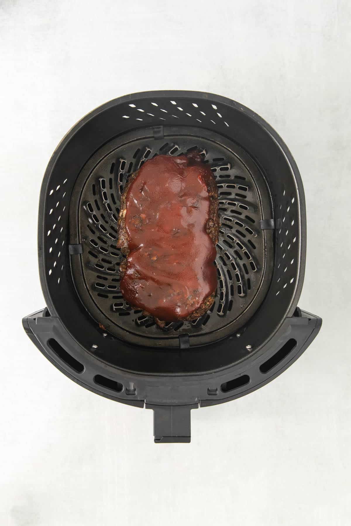 A meatloaf with sauce on top in an Air Fryer basket.