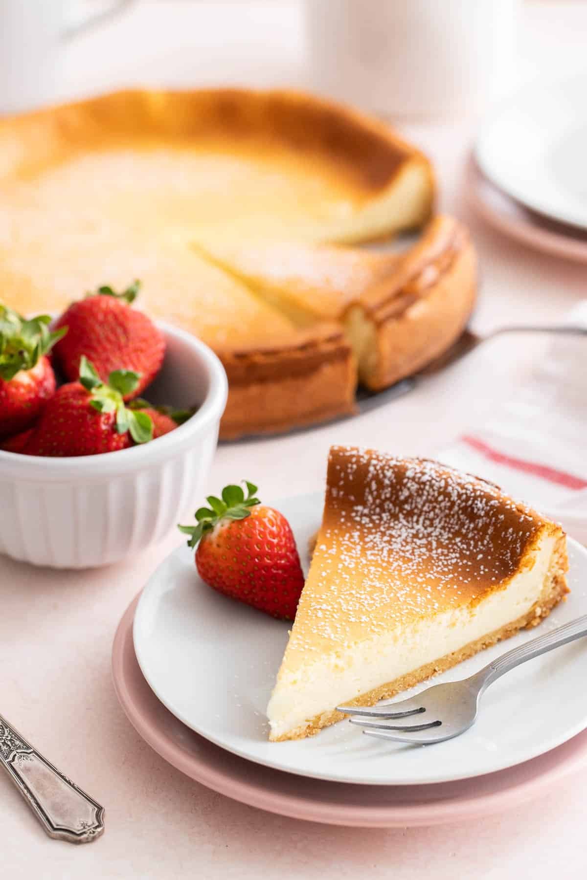 A cheesecake on a cake stand with a slice of cake in front of it.