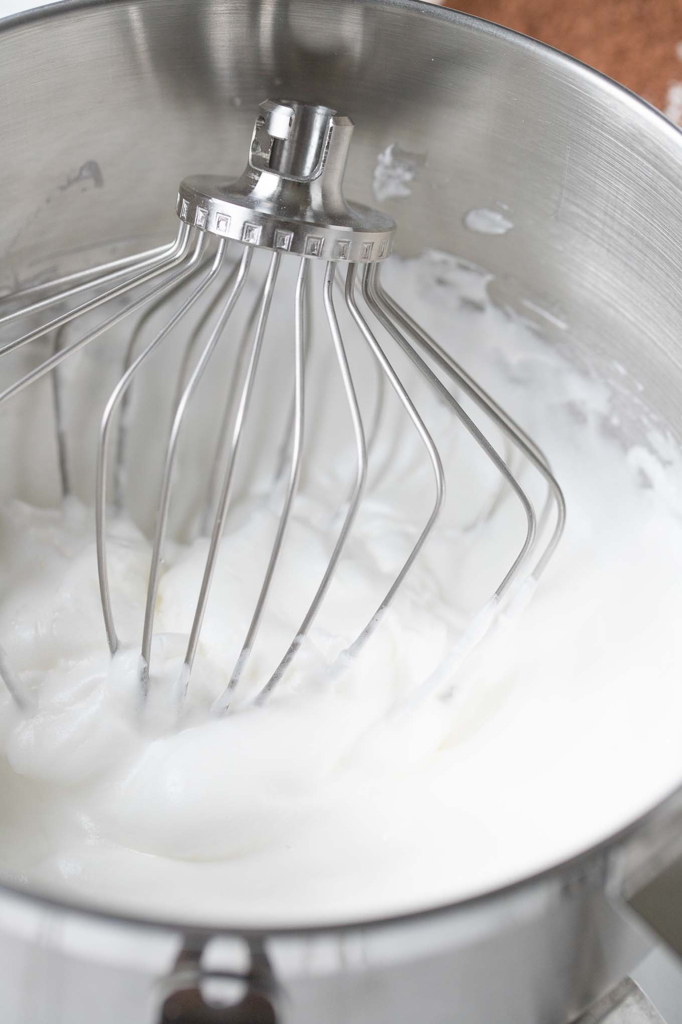 Whipped egg whites in a bowl with a whisk.