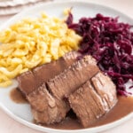 Sauerbraten on a white plate with spaetzle and red cabbage.