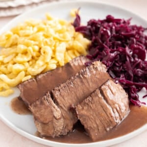Sauerbraten on a white plate with spaetzle and red cabbage.