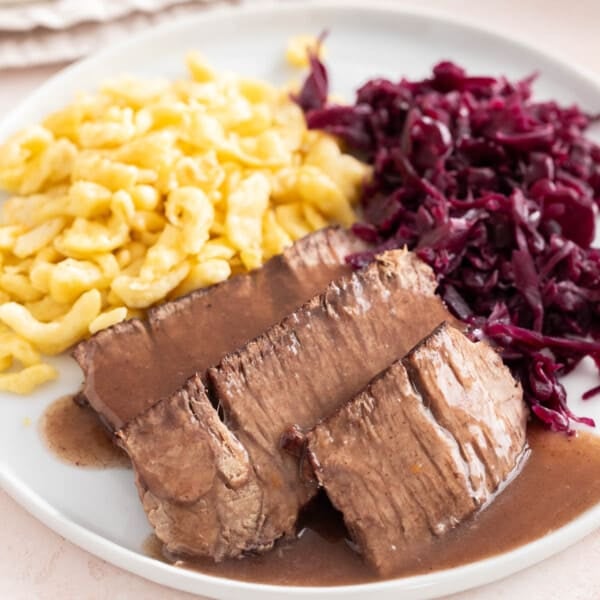 Sauerbraten on a white plate with spaetzle and red cabbage.