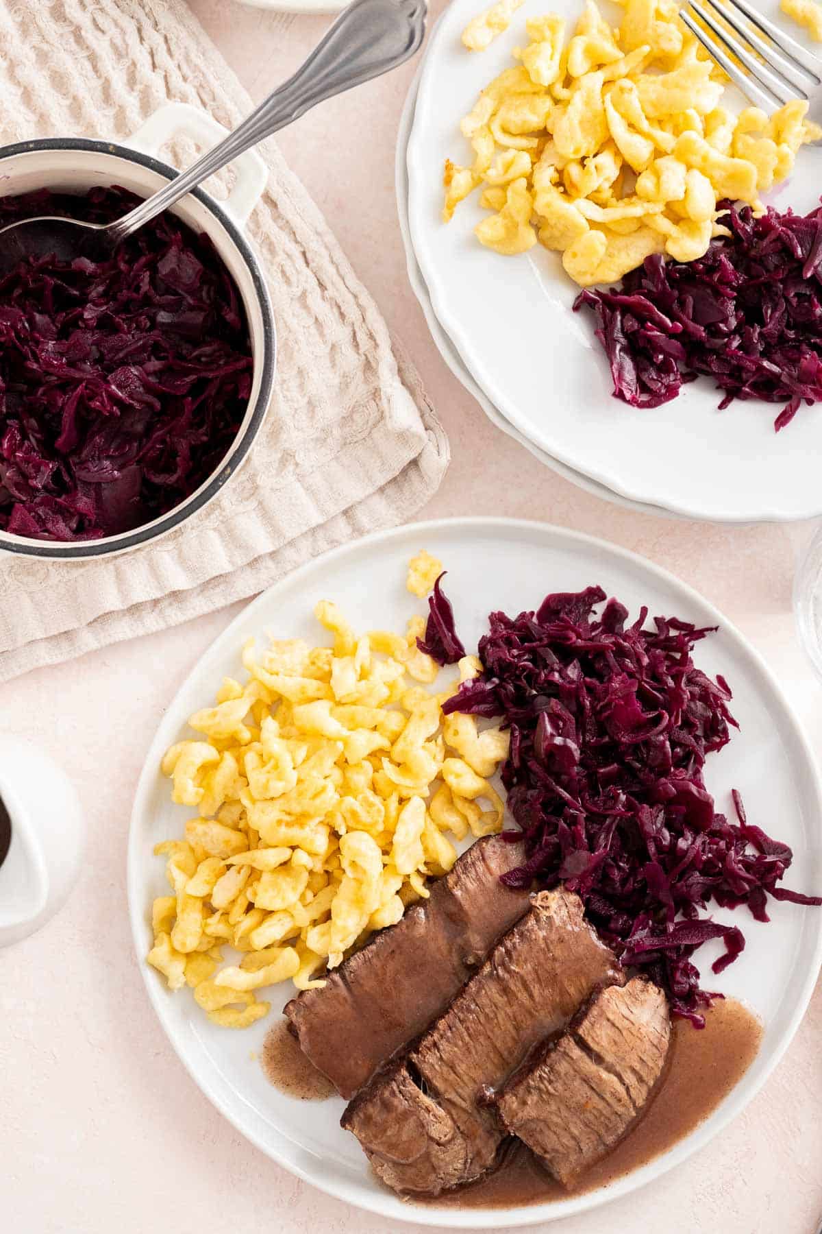 A sliced roast served on a white plate with Blaukraut in a serving dish next to it.