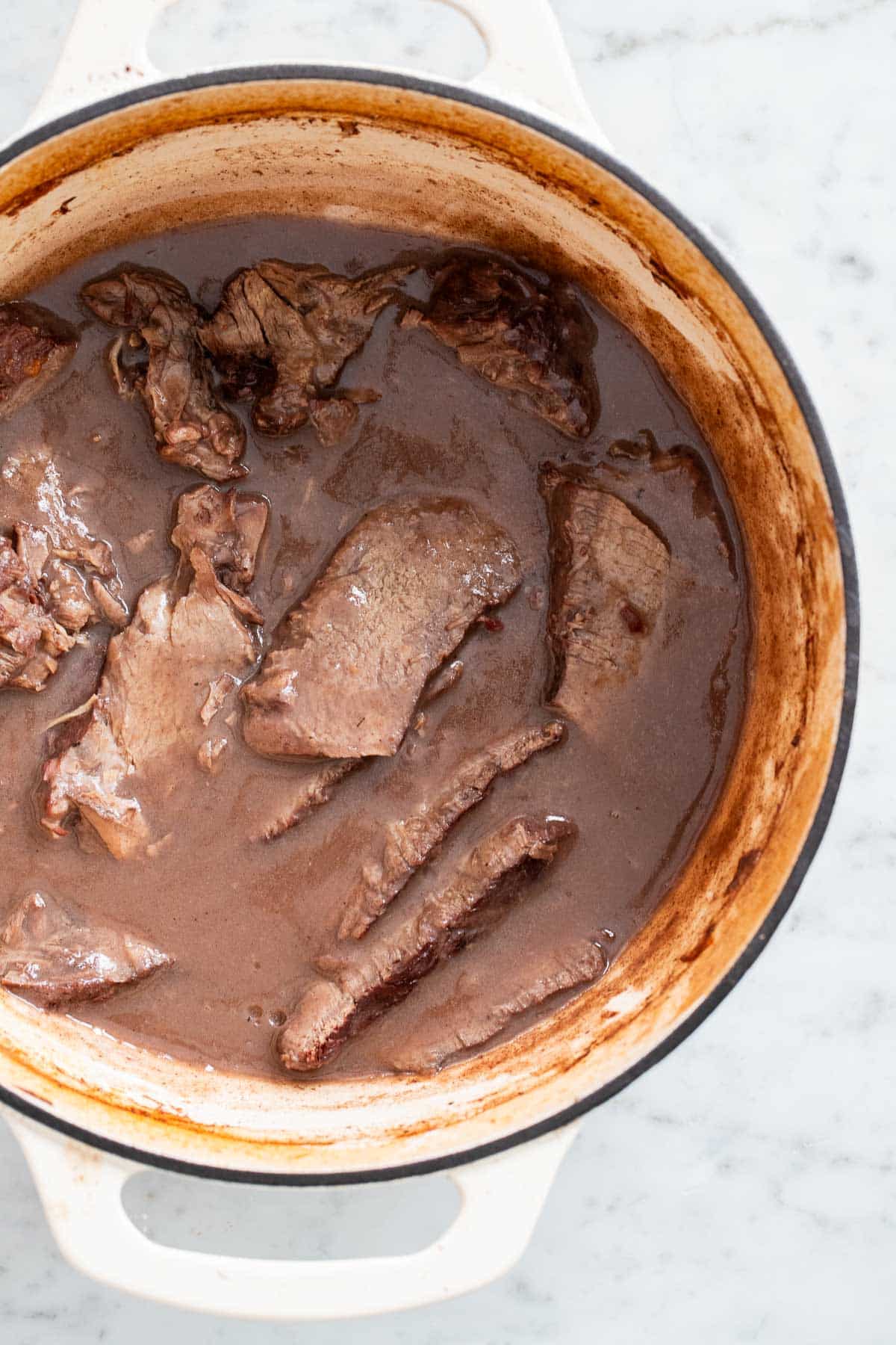 Sliced roast and gravy in a Dutch oven.