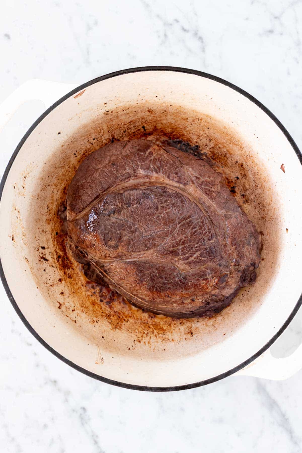 Seared roast in a white Dutch oven.