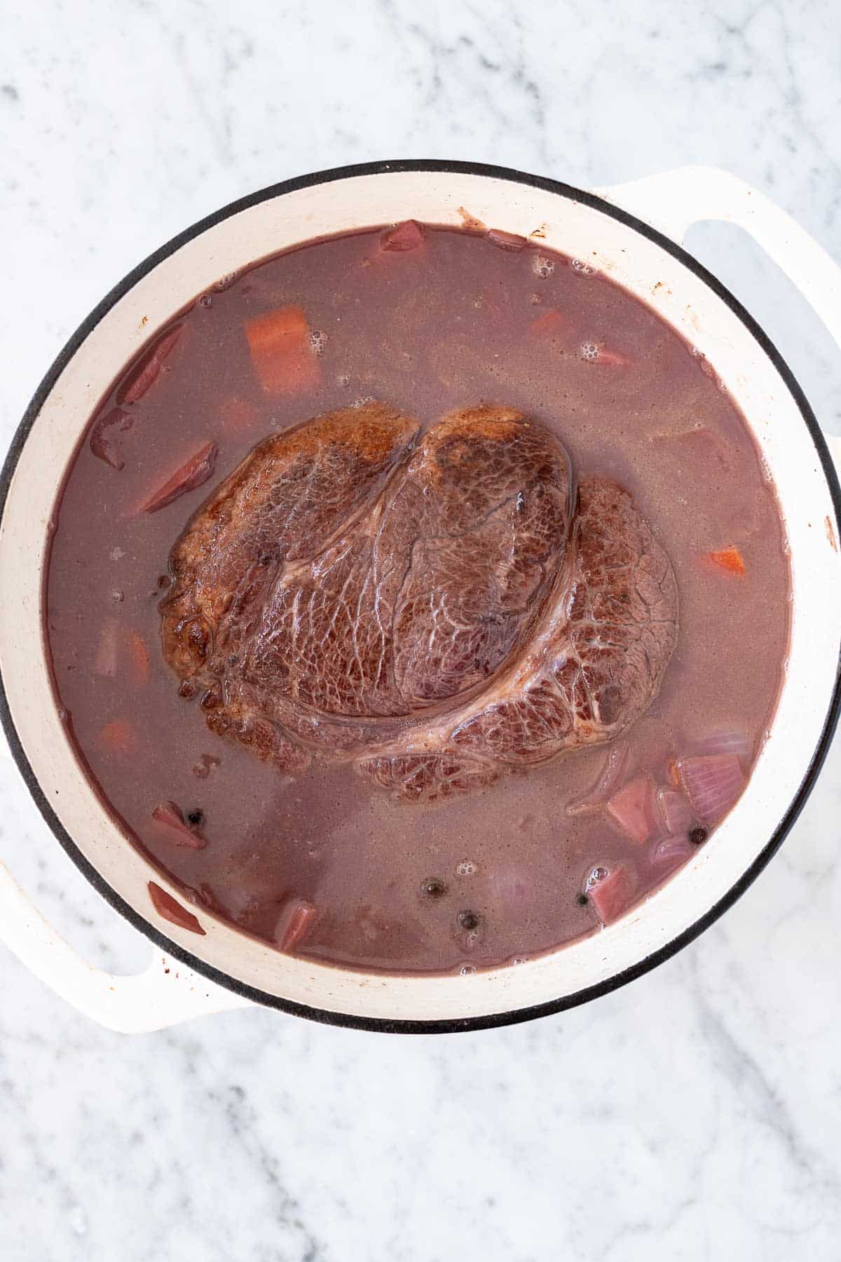 Roast, brine, and vegetables in a white dutch oven.