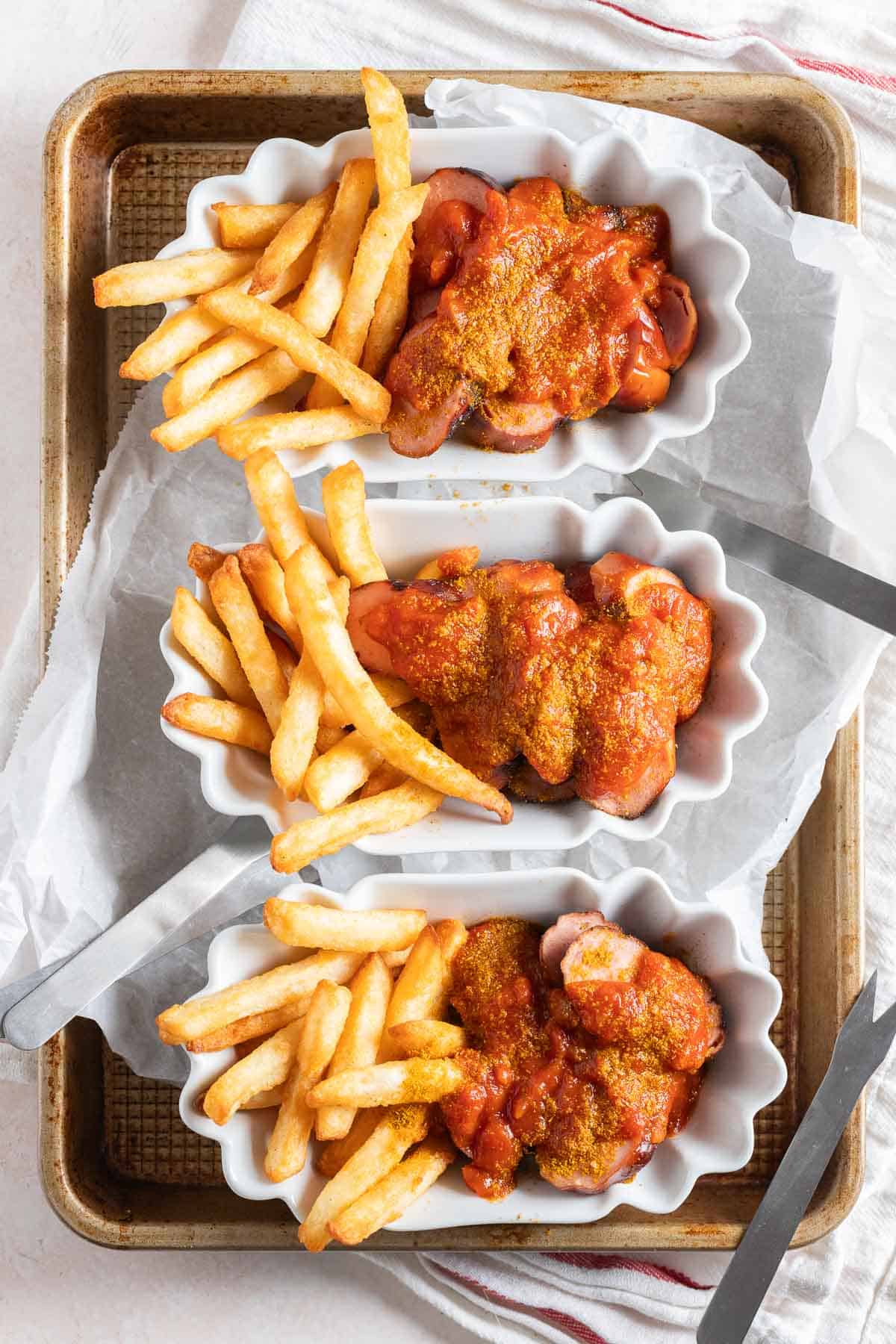Three white serving dishes filled with currywurst and fries.
