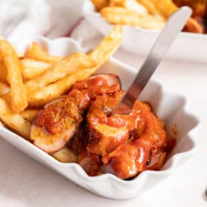 Currywurst with fries in a white serving dish.