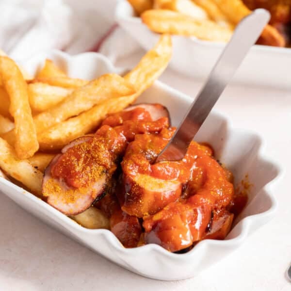 Currywurst with fries in a white serving dish.