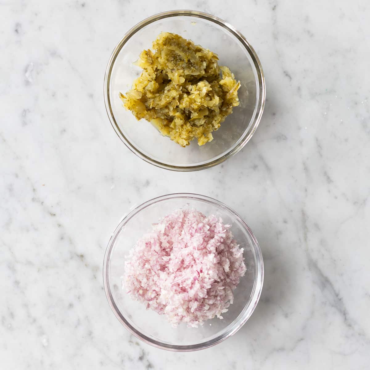 Finely chopped onions and pickles in two glass bowls.